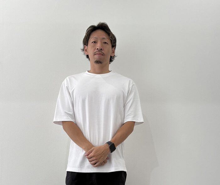 白いTシャツ姿でポーズをとる男性スタッフ（エヌルーム訪問看護ステーション）