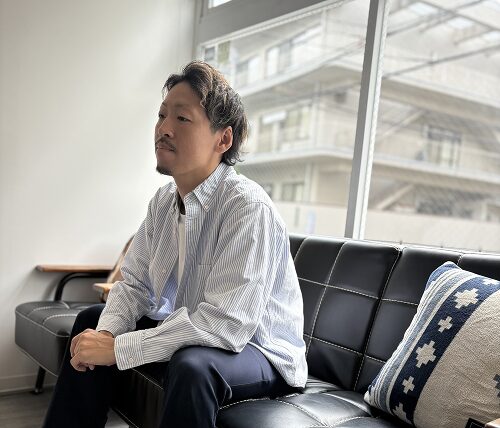 白いTシャツ姿でソファーに腰掛ける男性スタッフ（エヌルーム訪問看護ステーション）